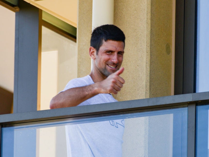 Novak Djokovic smiles to photographers from one of the hotels where players are quarantined