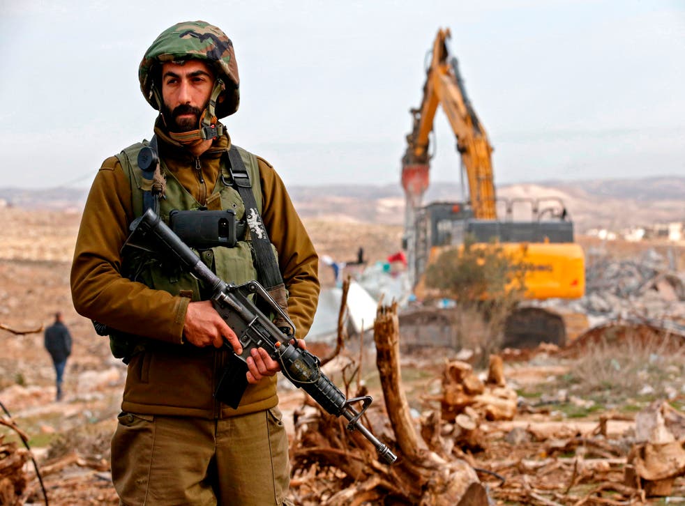 An Israeli soldier stands guard as an excavator demolishes a Palestinian home which Israeli authorities said was build without a permit in the village of Al-Dirat near the West Bank town of Hebron on 16 January, 2020. The Israeli government has approved the construction of hundreds of new homes in West Bank settlements.