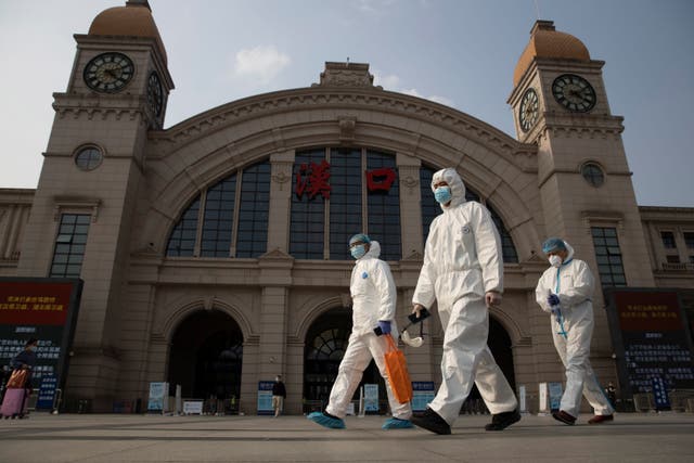 <p>Workers in protective suits walk through central Wuhan</p>