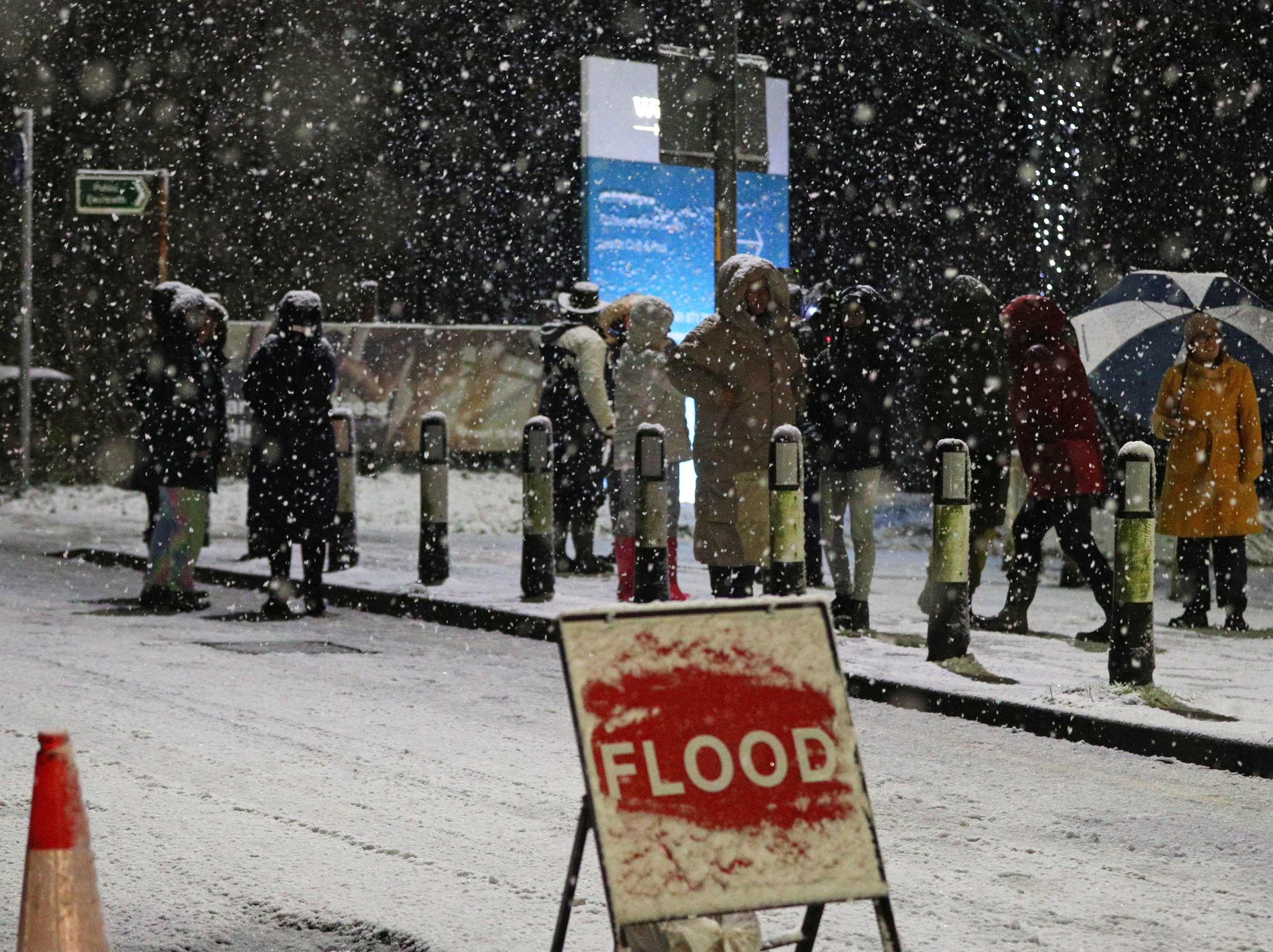 People cross a bridge over the River Mersey as snow falls in East Didsbury, Manchester, where homes are being evacuated due to risk of flooding
