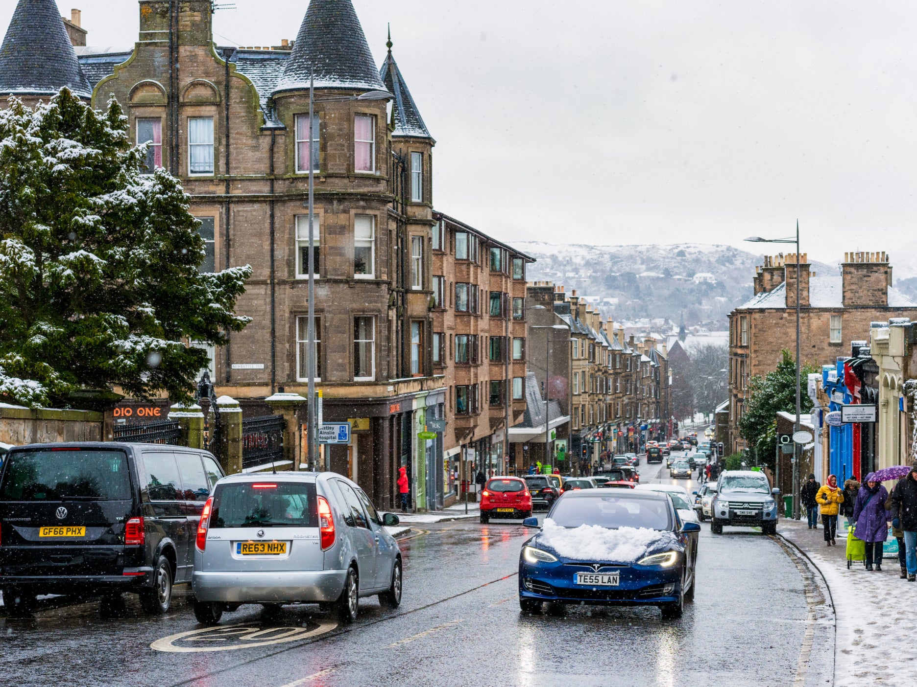A Tesla electric car drives through the snowy streets of Edinburgh. The Scottish government is rolling out more charging points but also encouraging fewer car journeys