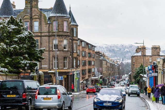 A Tesla electric car drives through the snowy streets of Edinburgh. The Scottish government is rolling out more charging points but also encouraging fewer car journeys