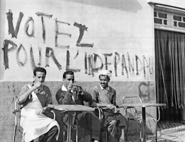 Algerians drinking coffee under a wall covered with pro-independence graffiti in 1962