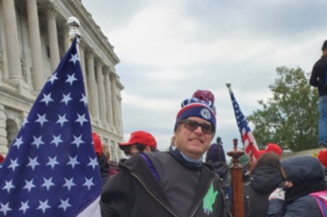 <p>Dustin Thompson allegedly posing with a coat rack from the US Capitol, according to a Department of Justice affidavit</p>