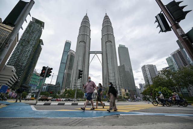 <p>Los peatones cruzan una calle frente a las emblemáticas Torres Gemelas Petronas de Malasia en Kuala Lumpur el 12 de enero de 2021&nbsp;</p>