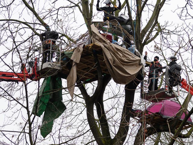An environmental protestor (second from right) waves from a cherry picker as he is removed from his treetop position, as bailiffs and police officers clear the site of a “Stop HS2” camp at Euston Station