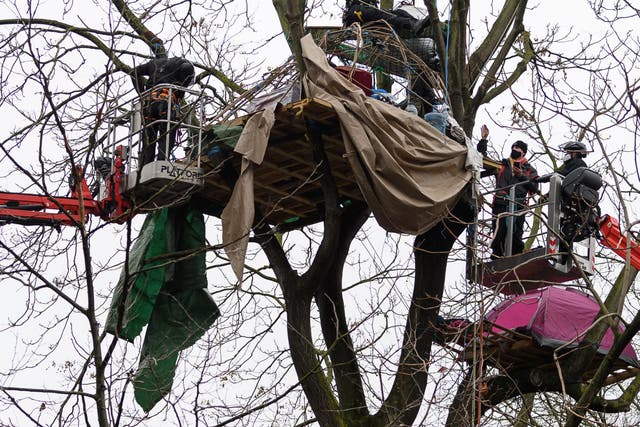An environmental protestor (second from right) waves from a cherry picker as he is removed from his treetop position, as bailiffs and police officers clear the site of a “Stop HS2” camp at Euston Station
