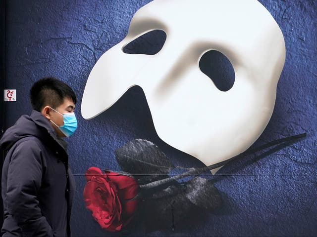  A man wears a face mask as he walks pasta a Phantom of the Opera poster in Manchester