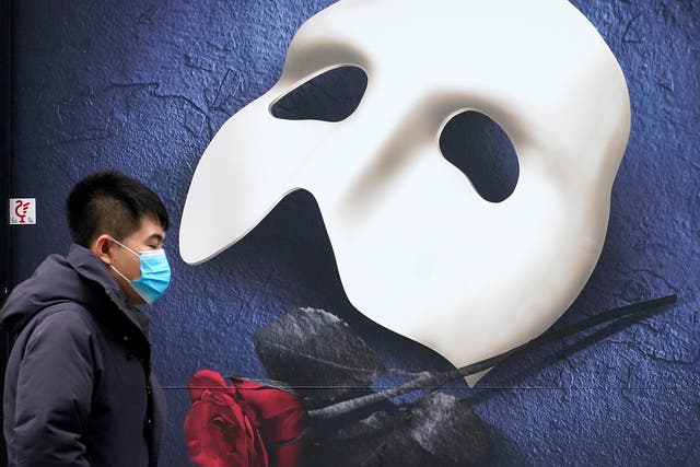 <p>A man in a mask passes a ‘Phantom of the Opera’ poster in Manchester</p>