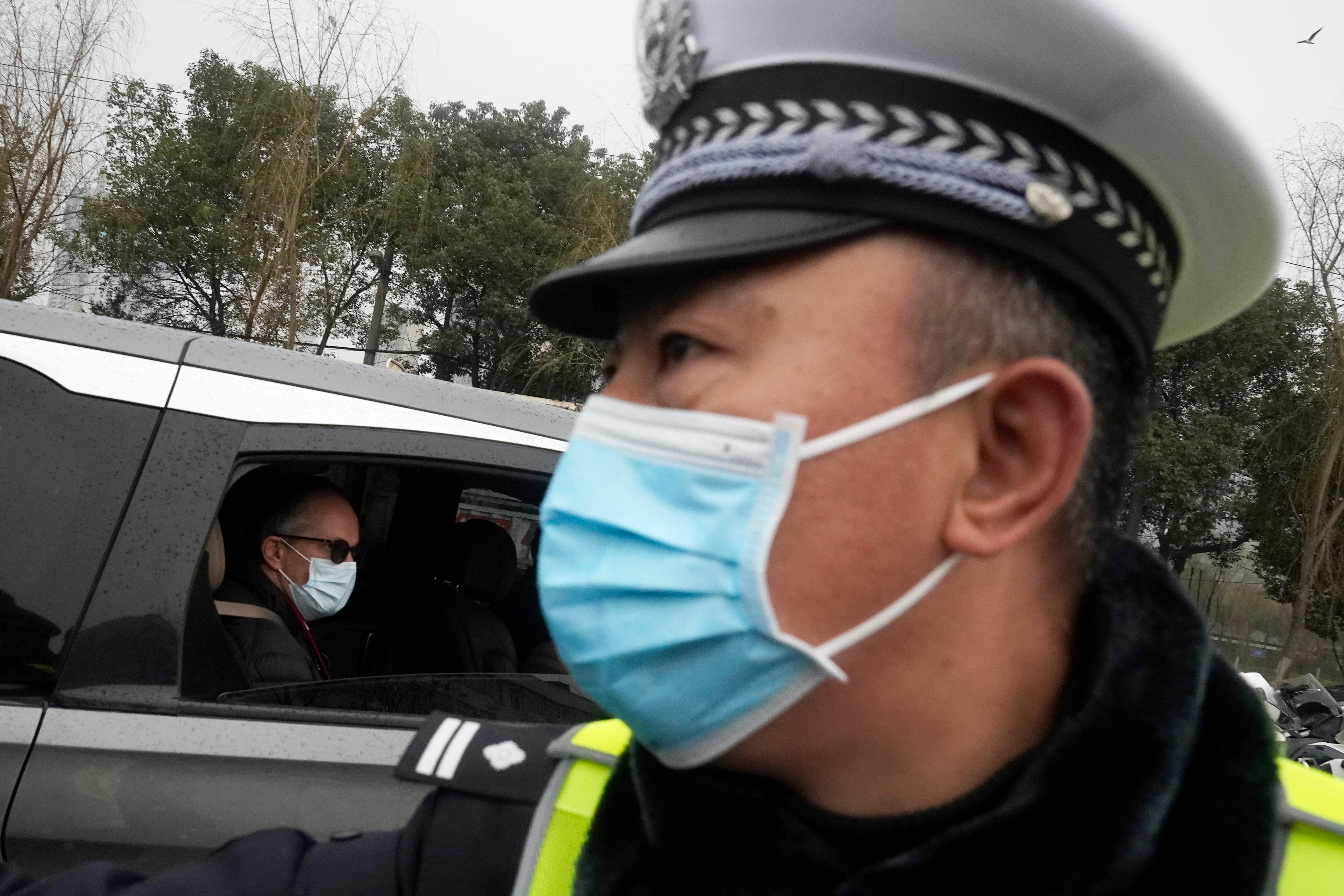 <p>Peter Ben Embarek. del equipo de la Organización Mundial de la Salud, pasa junto a un policía chino a su salida en una caravana del mercado de alimentación de Baishazhou, en el tercer día de visitas sobre el terreno en Wuhan, en la provincia china de Hubei, el domingo 31 de enero de 2021.&nbsp;</p>
