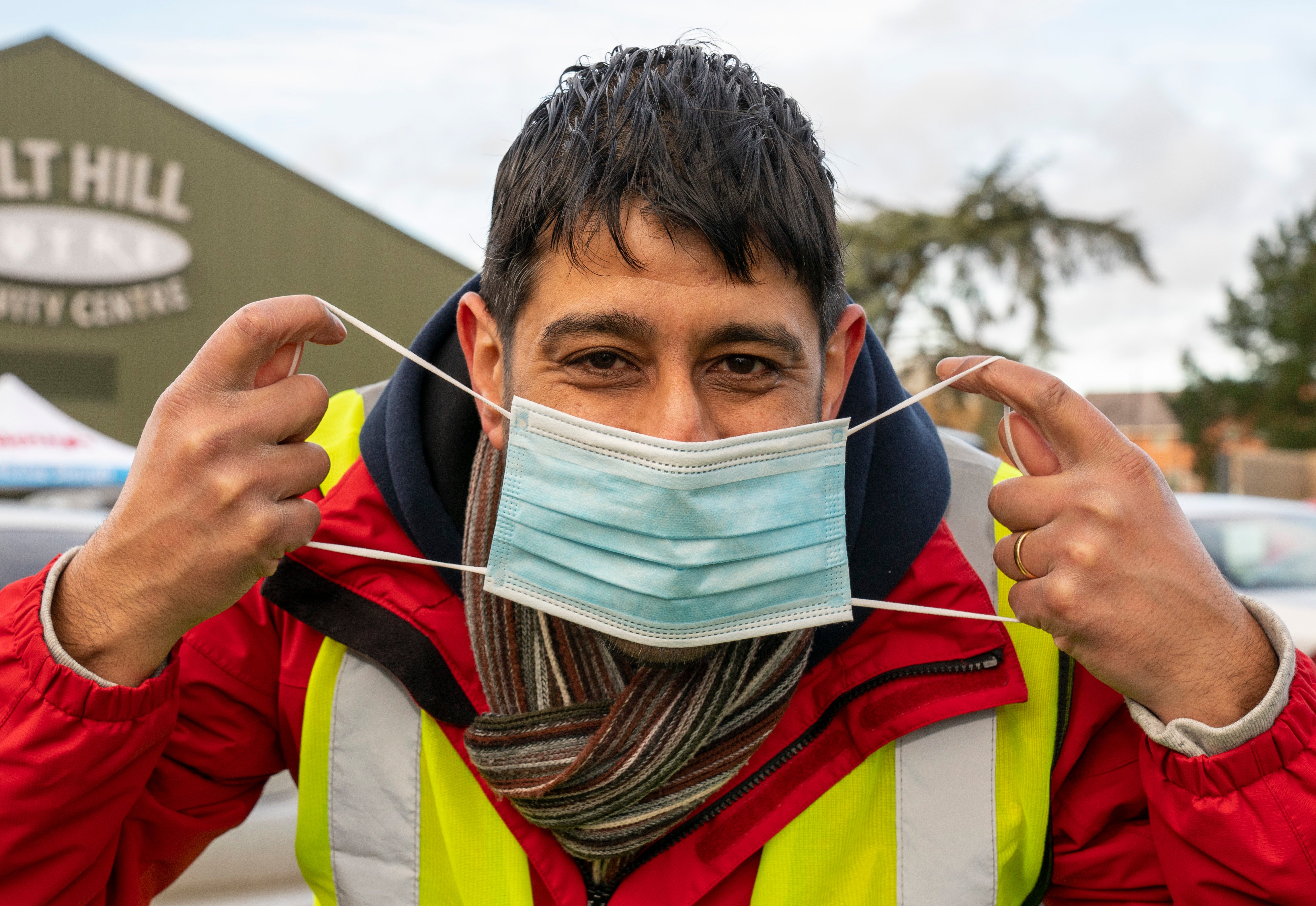 Volunteer Rajan Bindra smiles with his eyes welcoming patients at a vaccination centre in Slough