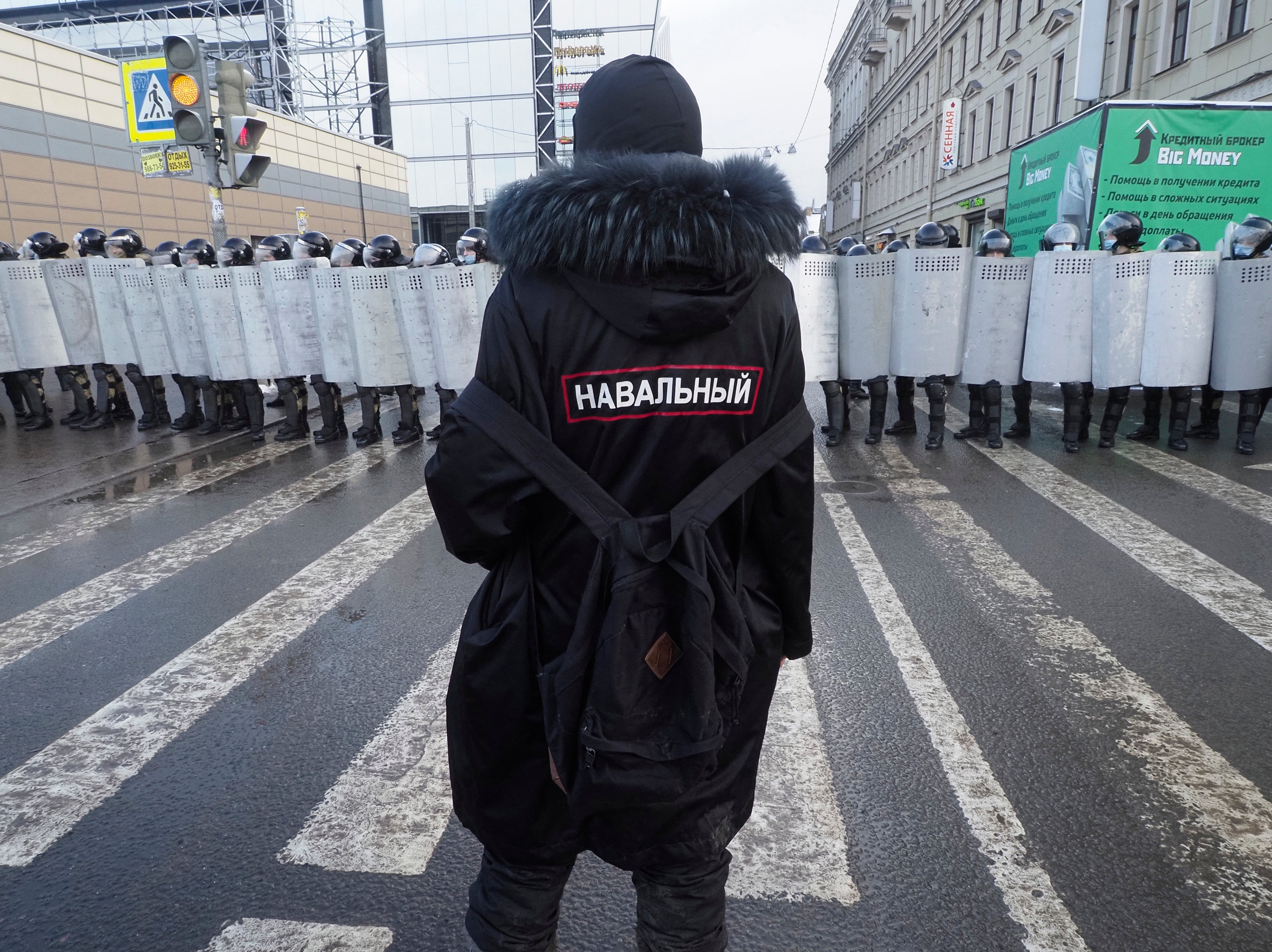A man with a sign ‘Navalny’ on his back stands in front of riot policemen blocking the way to protester during a protest against the jailing of opposition leader Alexei Navalny in St. Petersburg
