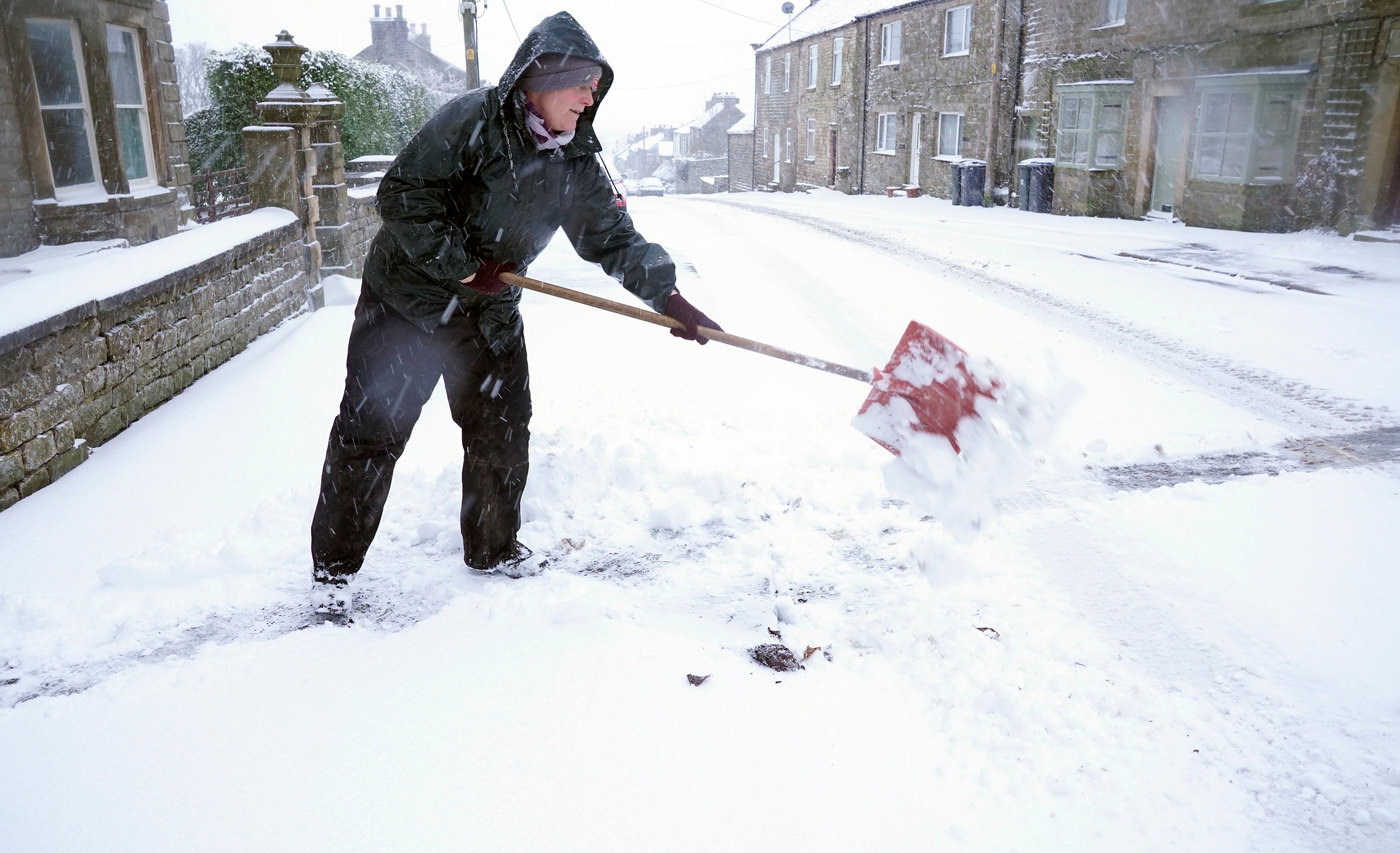 A woman clears her path in Bowes in County Durham as heavy snow falls.
