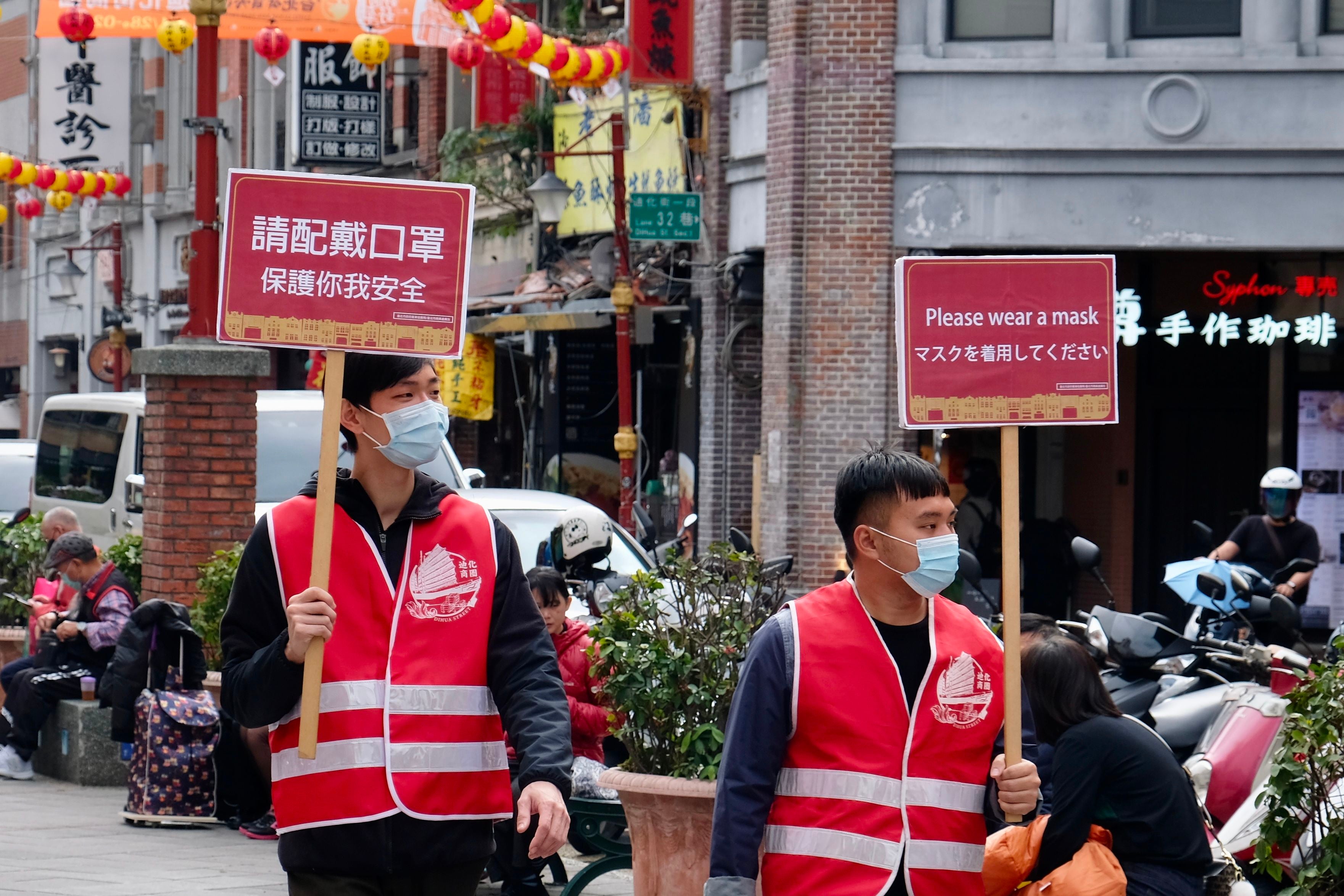 File: Two volunteers walk around the Dihua traditional market with signs calling for people to wear masks in Taipei on Tuesday
