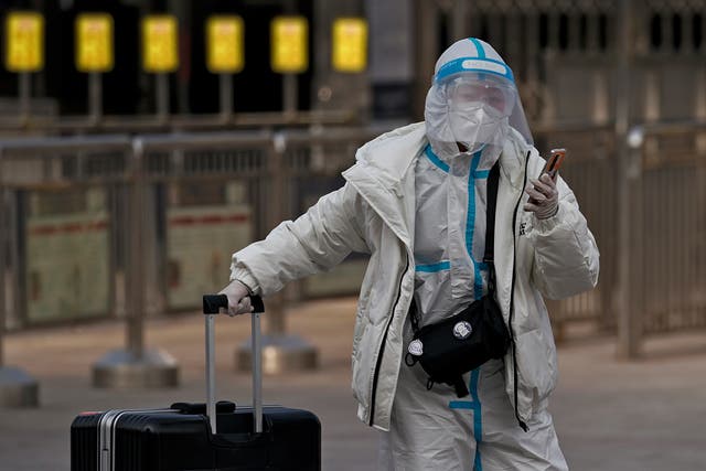 <p>Una mujer, con un traje de protección en plena pandemia del coronavirus, llega con una maleta a tomar un tren, en la estación de tren de Beijing, el 27 de enero de 2021.&nbsp;</p>
