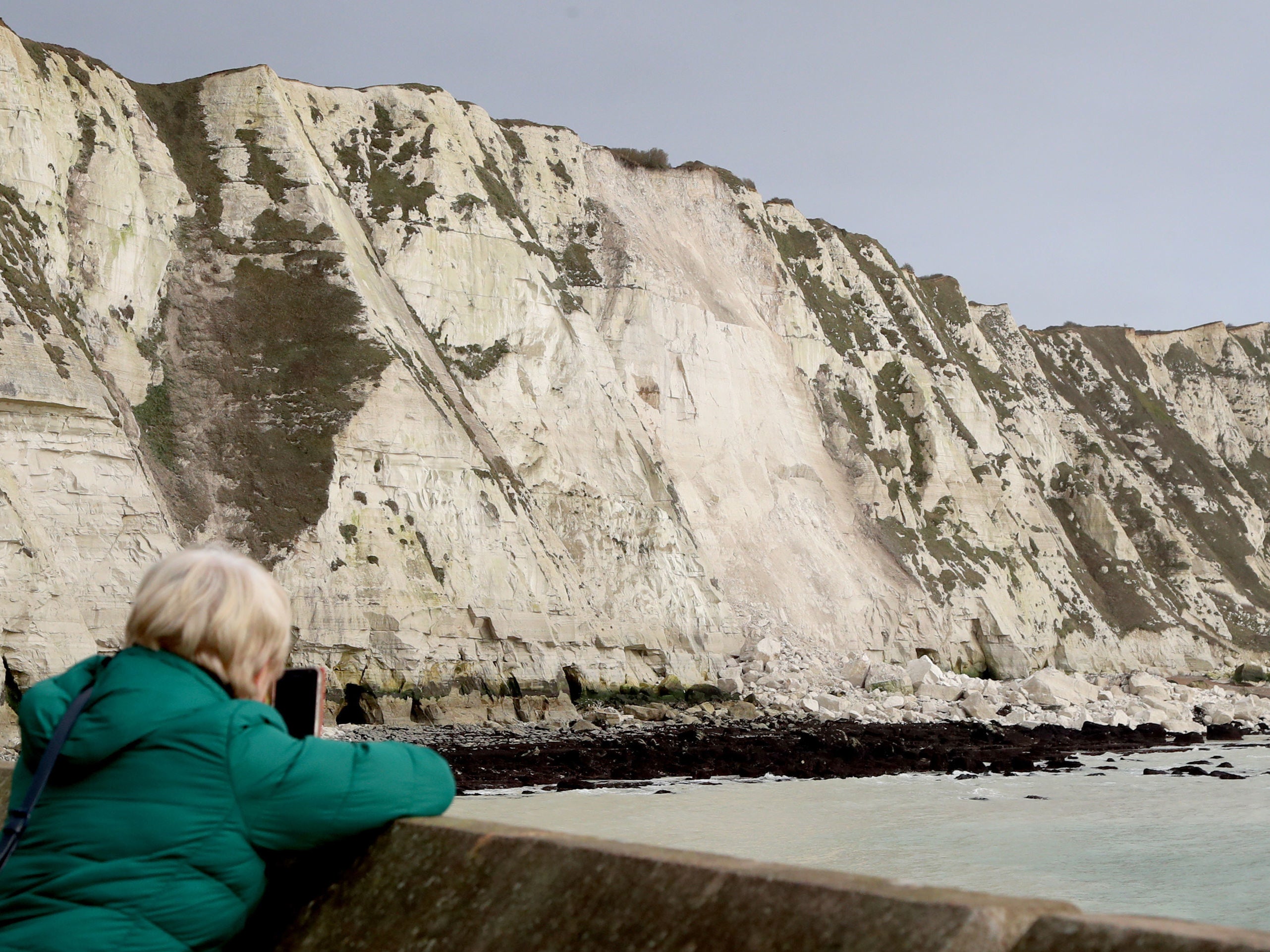 <p>A woman takes a picture of the White Cliffs of Dover in Kent, following a cliff fall yesterday, thought to have been caused by a combination of high winds and freezing rain being absorbed into the chalk and then expanding, causing the cliff to weaken</p>