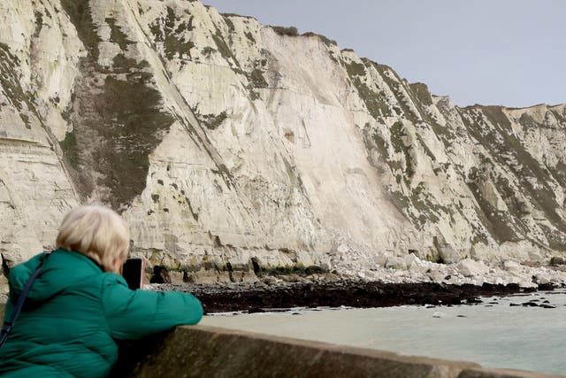 <p>A woman takes a picture of the White Cliffs of Dover in Kent, following a cliff fall yesterday, thought to have been caused by a combination of high winds and freezing rain being absorbed into the chalk and then expanding, causing the cliff to weaken</p>