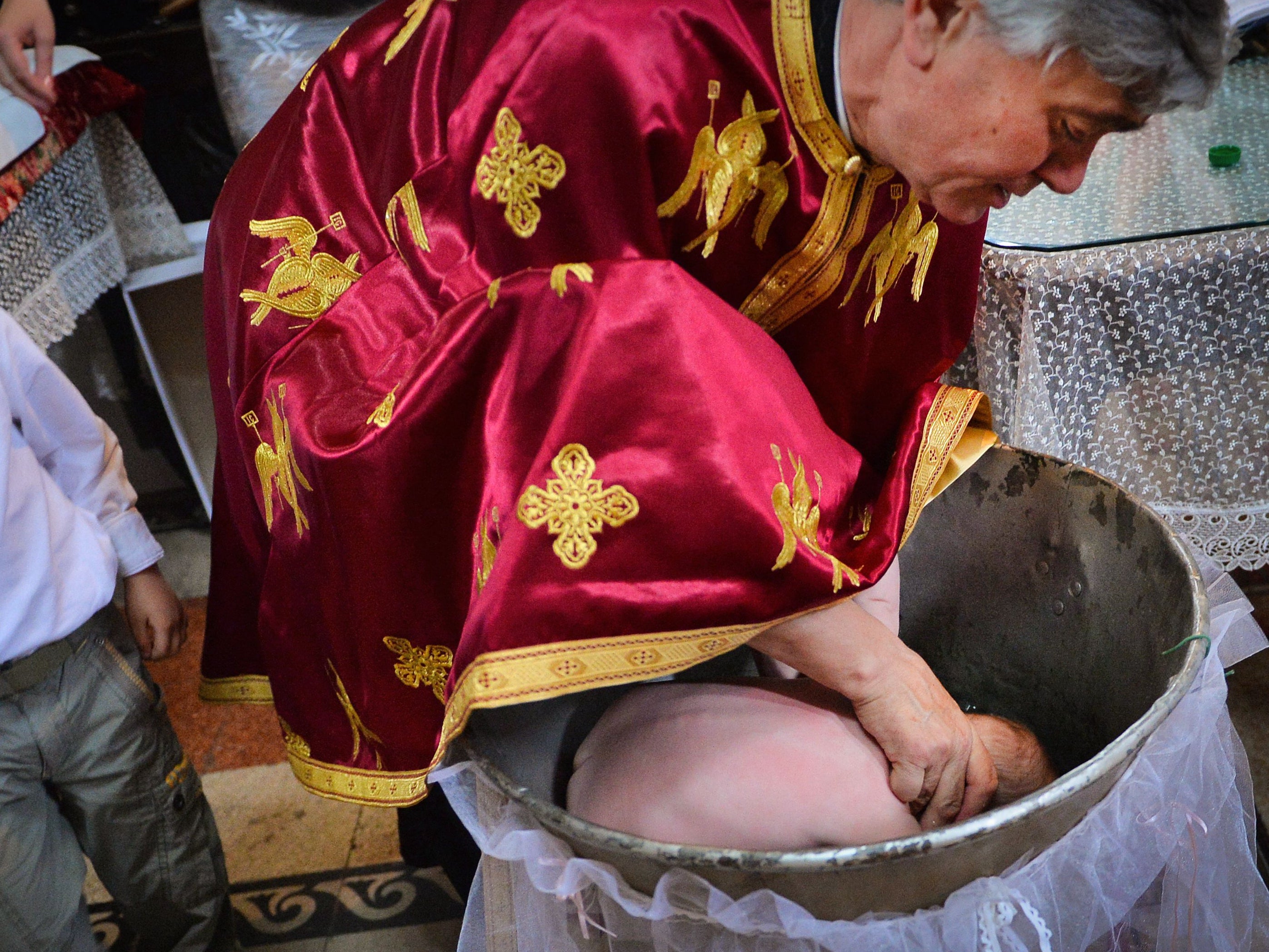 <p>A Romanian Orthodox priest sinking a child in holy water during baptism, in a church in Bucharest</p>