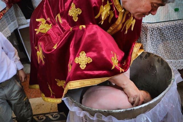 <p>A Romanian Orthodox priest sinking a child in holy water during baptism, in a church in Bucharest</p>