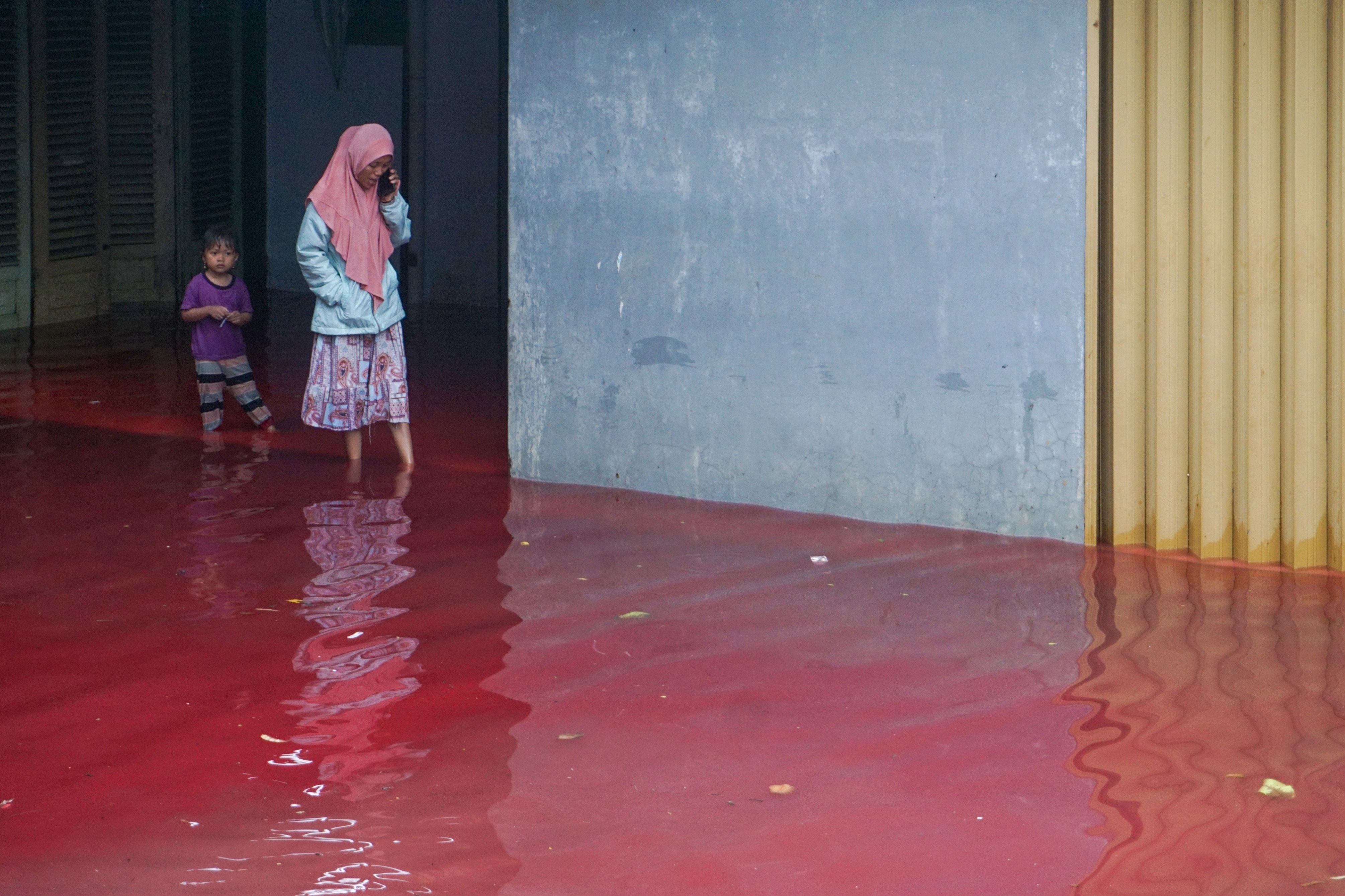 Residents wade through red floodwaters in Pekalonga