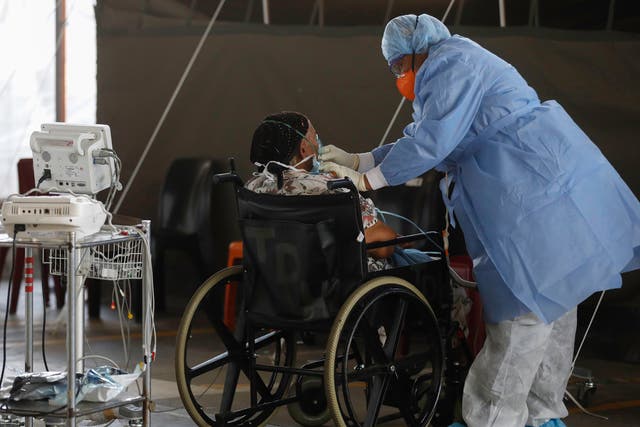 <p>A healthcare worker wearing personal protective equipment (PPE) stands next to a patient at the temporary wards dedicated to the treatment of possible COVID-19 coronavirus patients at Steve Biko Academic Hospital in Pretoria, South Africa, 19 January 2021</p>