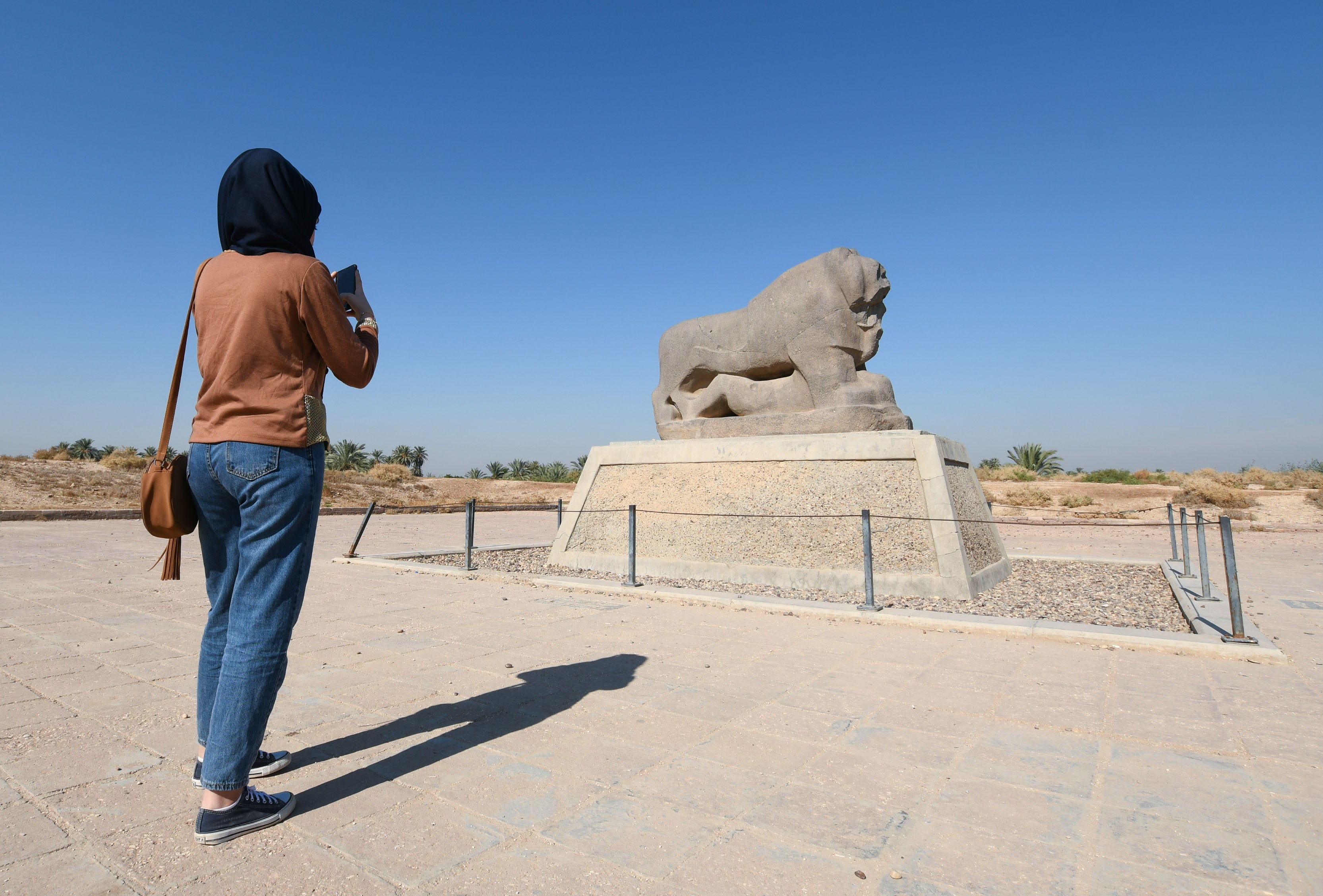 A visitor takes pictures of the statue of the Lion of Babylon