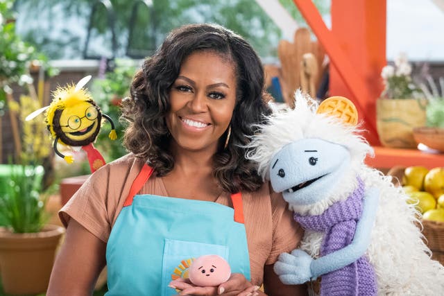 <p>This image released by Netflix shows former first lady Michelle Obama with Busy, a bee puppet, left, Mochi, a pink round puppet, and Waffles, a furry puppet with waffle ears on the set of the children’s series Waffles + Mochi</p>