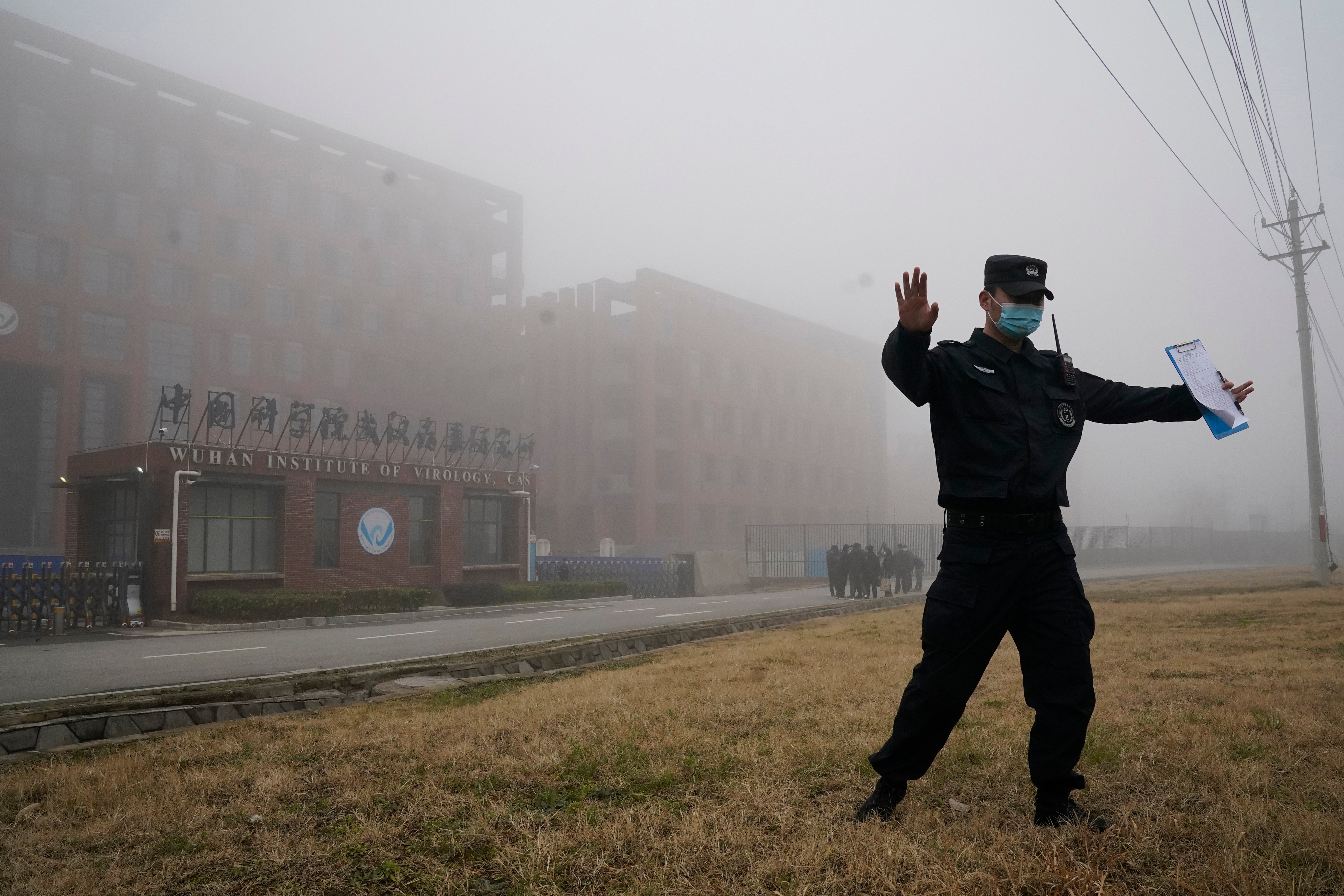 A security official moves journalists away from the Wuhan Institute of Virology after a World Health Organization team arrived for a field visit