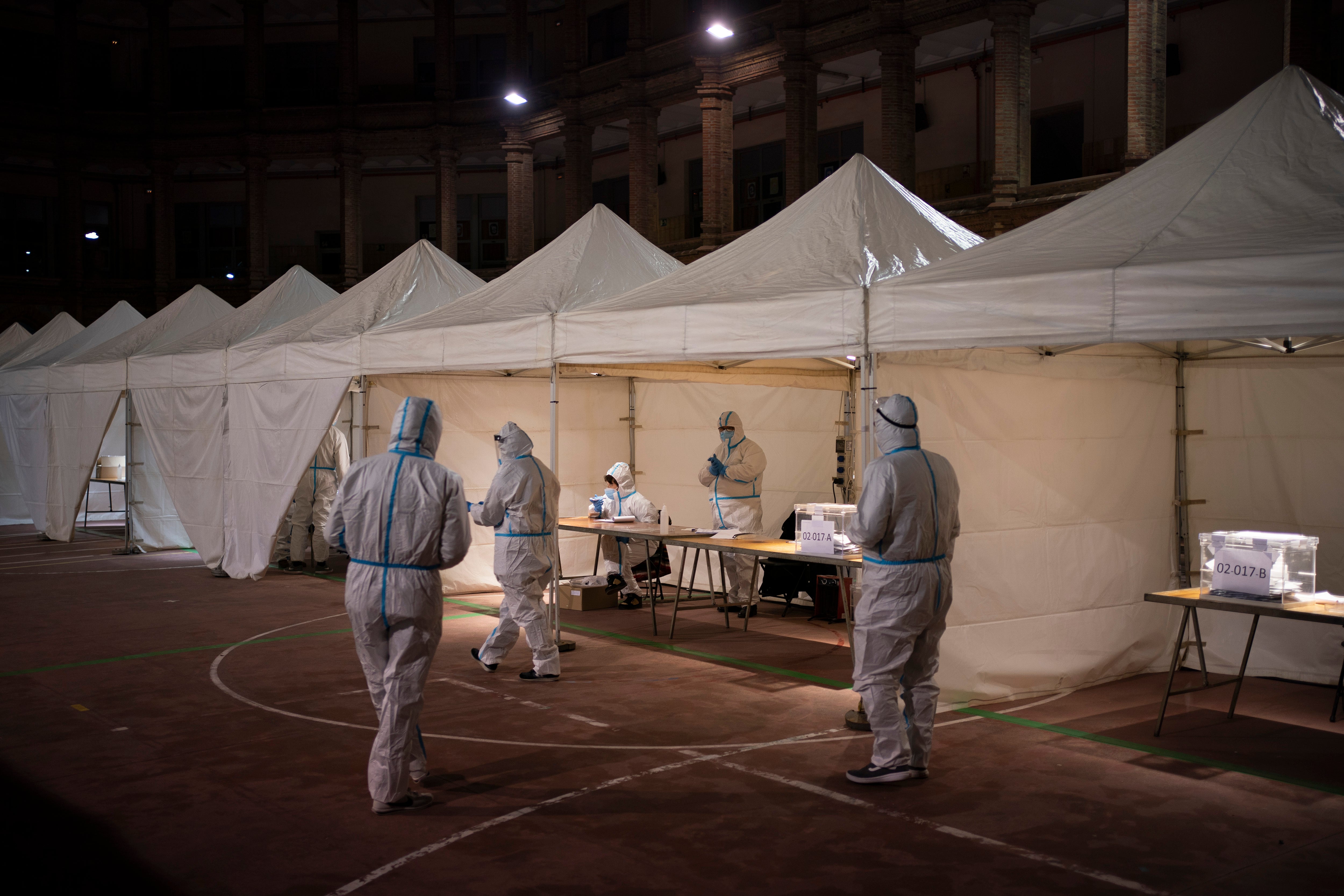 Electoral workers wearing protective suits wait for people to cast their vote at a polling station during the Catalan regional election in Barcelona on Sunday