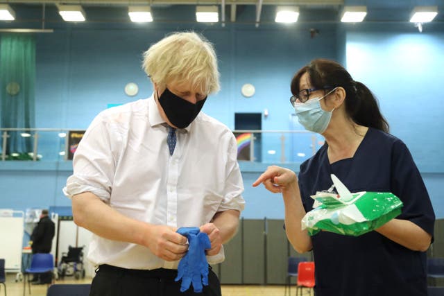 <p>El primer ministro británico, Boris Johnson (izq.), Habla con la trabajadora de salud Wendy Warren mientras se pone un par de guantes médicos mientras visita un centro de vacunación en el estadio Cwmbran en Cwmbran, Gales del Sur, el 17 de febrero de 2021.</p>