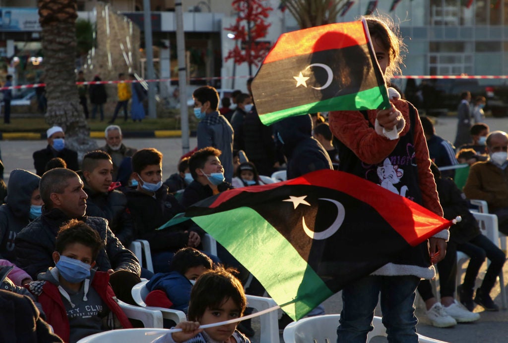 Libyan youths lift national flags as they attend a military parade on the eve of the 10th anniversary of the revolution in the port city of Tajoura