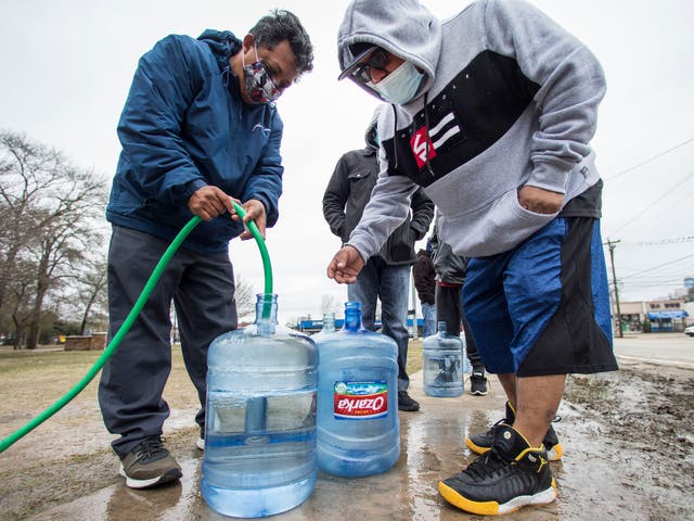 Victor Hernandez and Luis Martinez fill their water containers with a hose from a spigot in Haden Park in Houston, Texas, on Thursday 18 February 2021