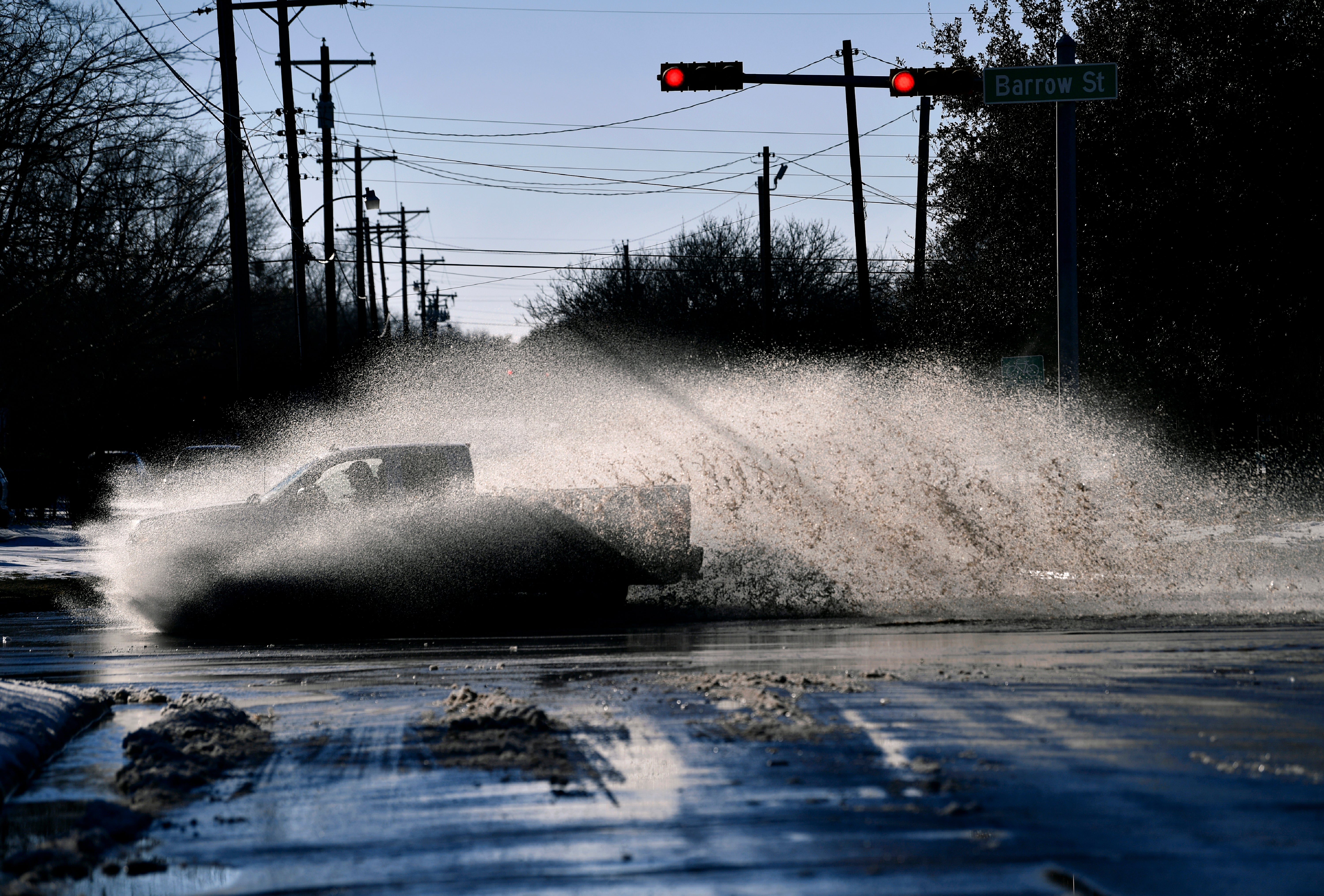 A pickup sends a wake of snow melt high into the air as the driver plows through a large puddle at Barrow and South 11th streets intersection in Abilene, Texas
