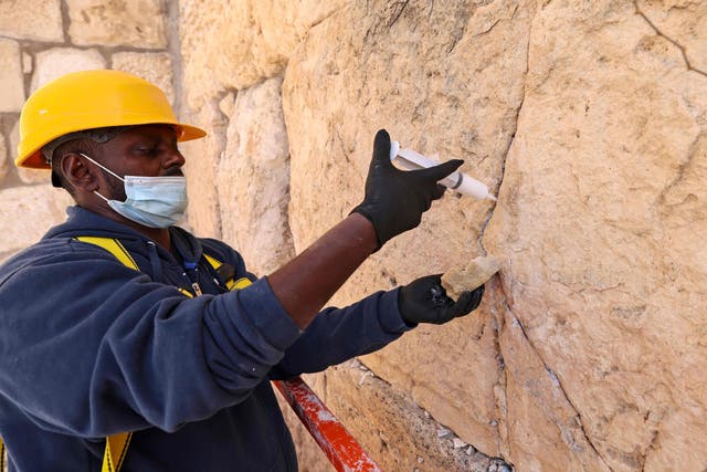 A worker of the Israeli Antiquities Authority uses a syringe to fill fissures in boulders at the Western Wall