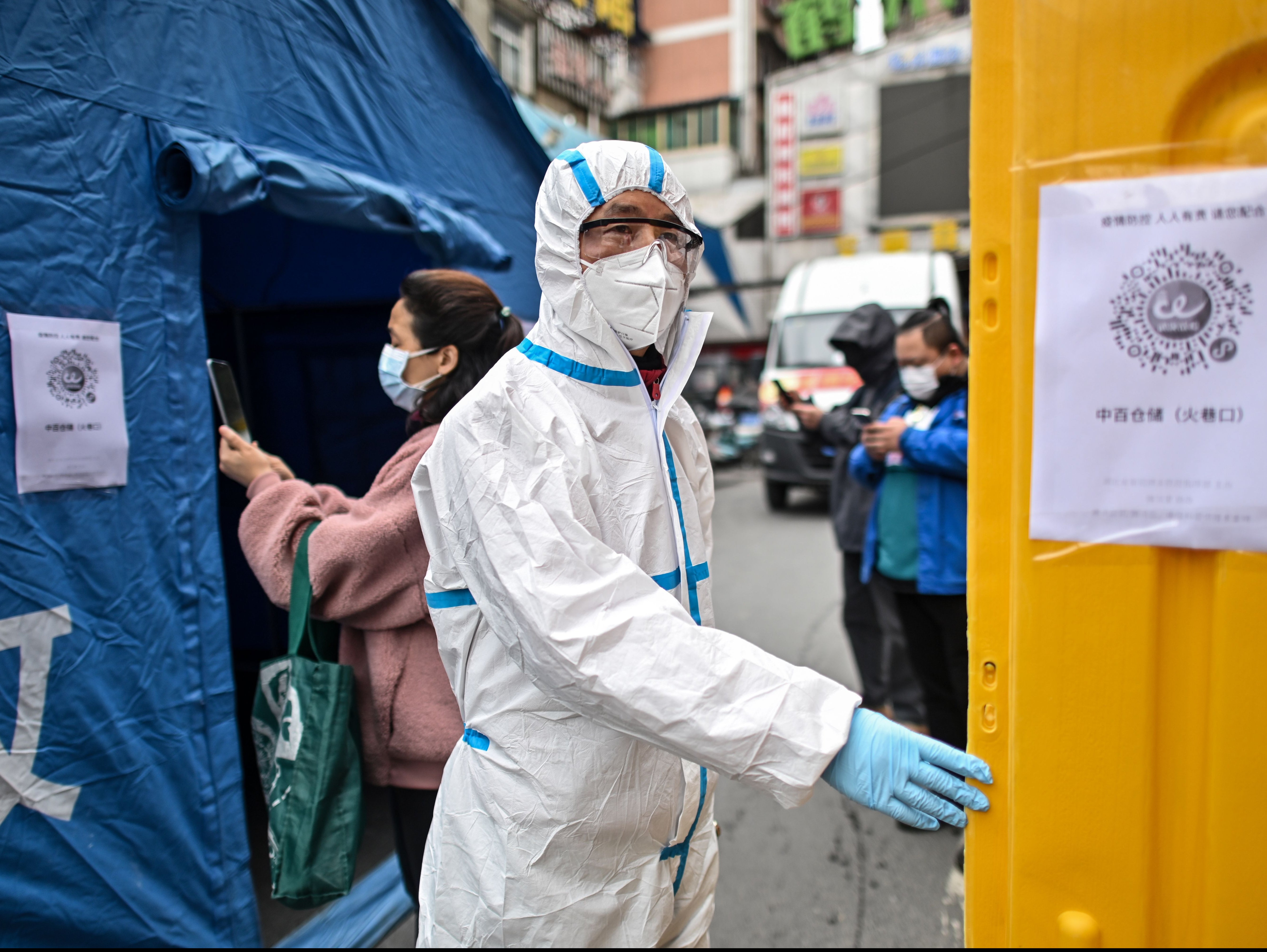 <p>A man wearing a protective suit controls the access to a market in Wuhan in March 2020</p>