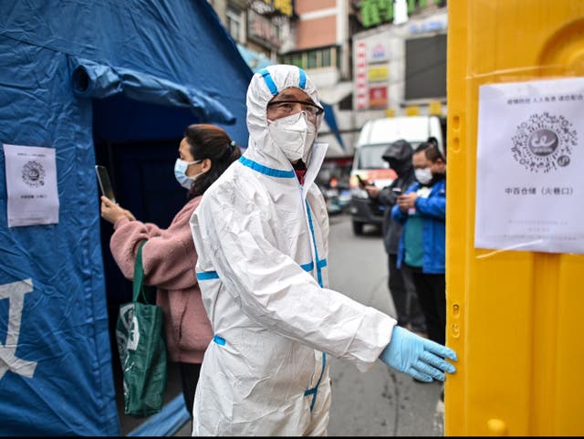 <p>A man wearing a protective suit controls the access to a market in Wuhan in March 2020</p>