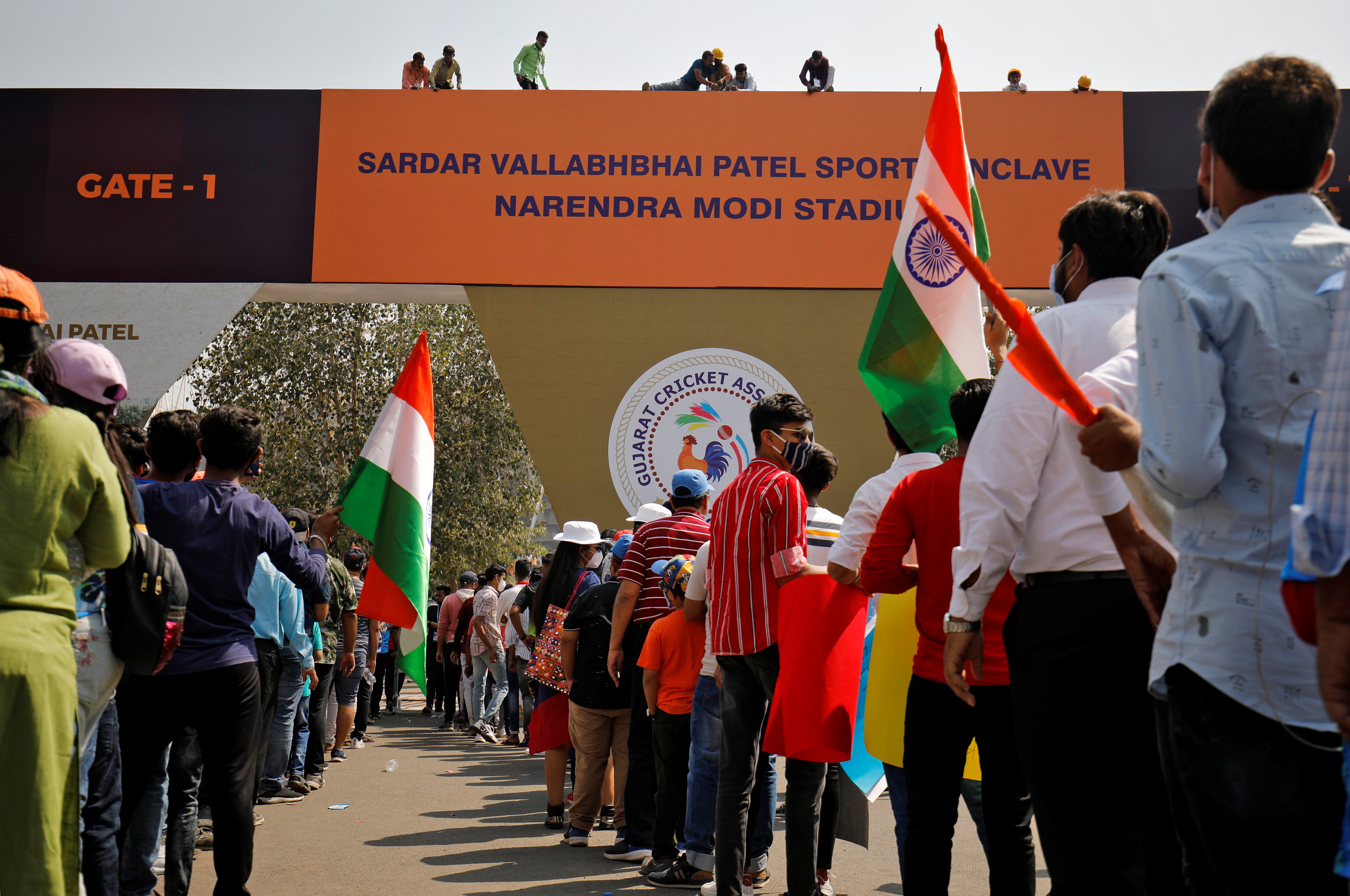 Workers install a hoarding renaming the world’s largest cricket stadium after Narendra Modi, even as fans wait to enter before the start of the third Test match between India and England
