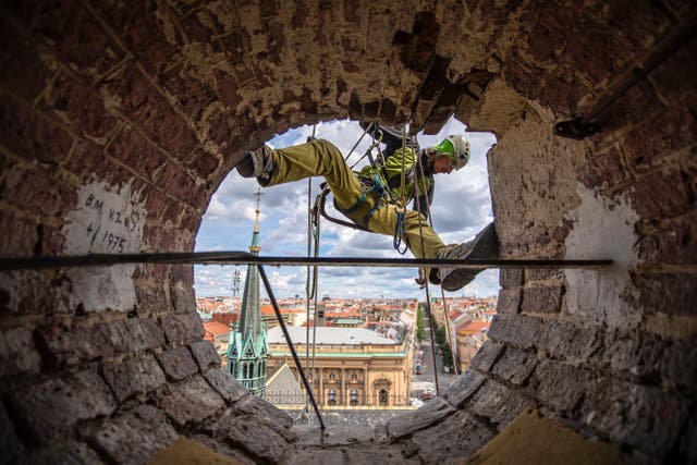 <p>A mountaineer carrying out maintenance work on the tower's clock at the Church of St Ludmila in Prague</p>
