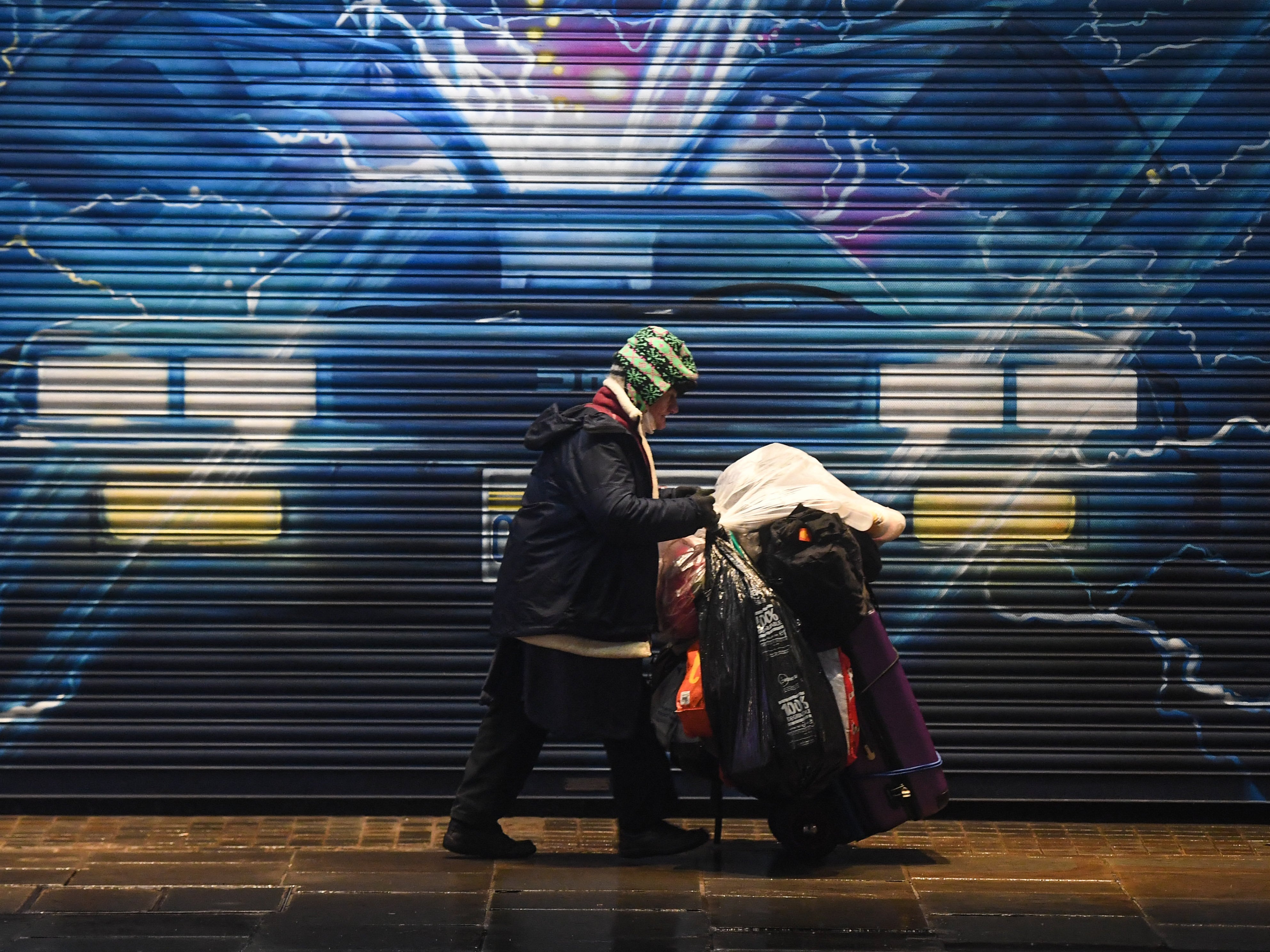 A rough sleeper pushes their belongings past a Back to the Future mural in London on 13 December