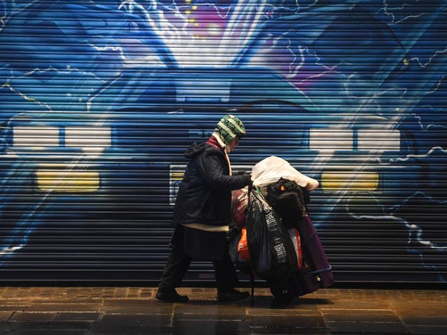 <p>A rough sleeper pushes their belongings past a Back to the Future mural in London on 13 December</p>