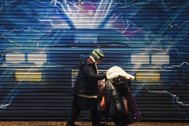 <p>A rough sleeper pushes their belongings past a Back to the Future mural in London on 13 December</p>