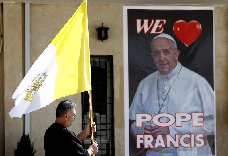 <p>Un sacerdote cristiano sostiene una bandera del vaticano mientras camina ante un cartel del papa Francisco, durante los preparativos para la visita del papa en Mar Youssif Church en Bagdad, Irak, el viernes 26 de febrero de 2021. </p>