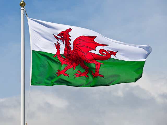 The welsh flag, a red dragon on a green and white background, flutters in the wind against a blue sky.