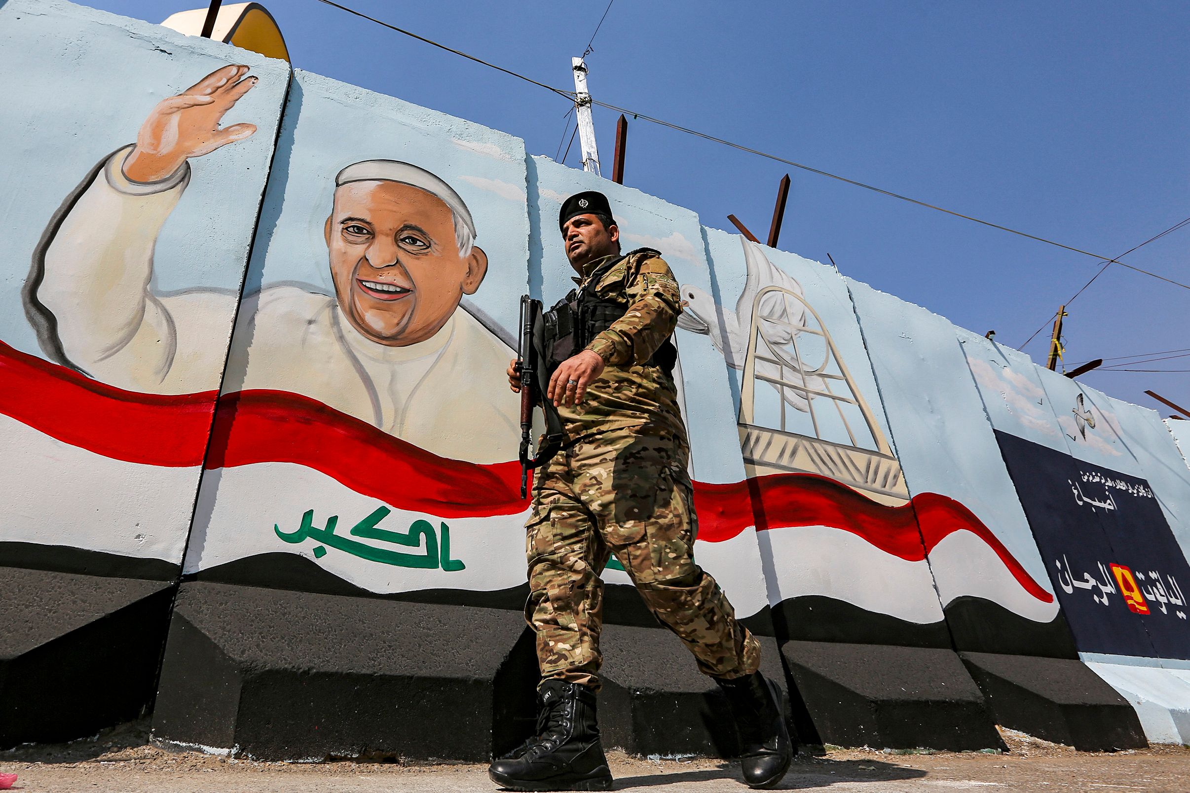 A member of the Iraqi forces walks past a mural depicting Pope Francis