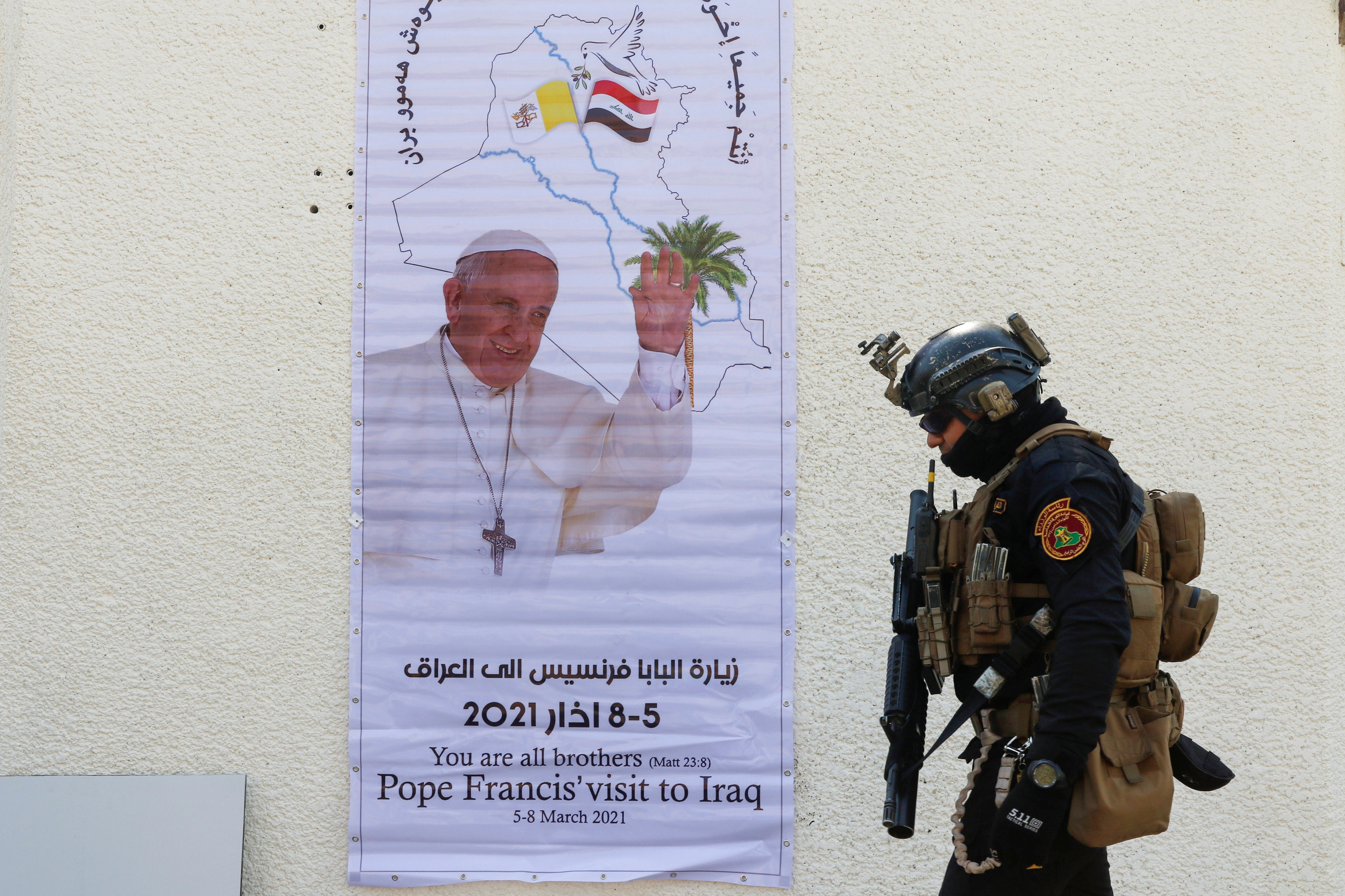 A security man walks near a poster of Pope Francis upon his upcoming visit to Iraq, in Baghdad