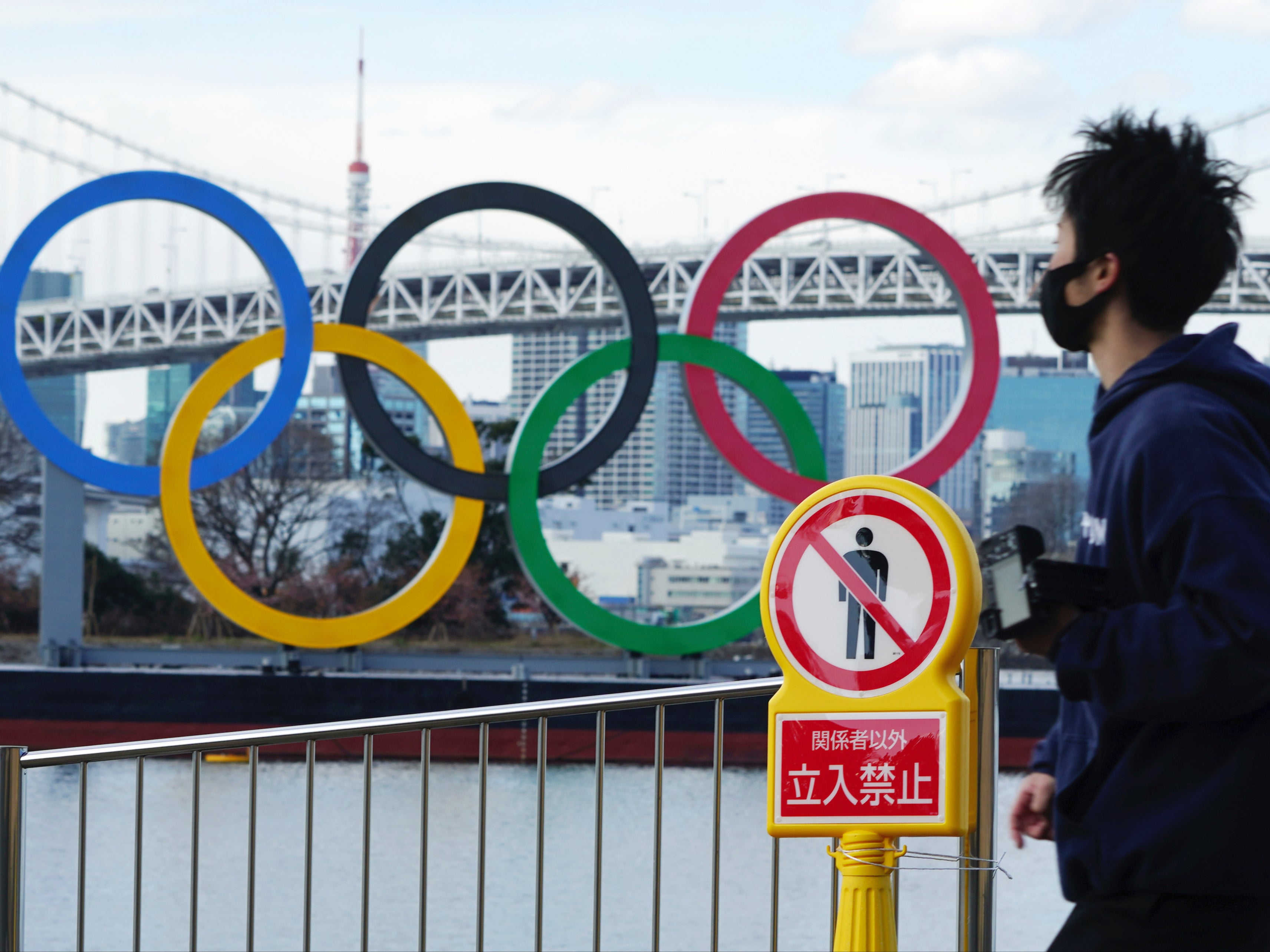 A man wearing a protective face mask walks near the Olympic rings