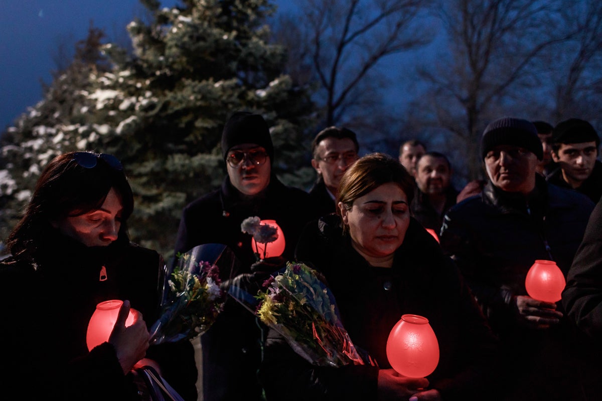 A group of relatives and friends of a killed soldier pray and listen to the words of a priest. People attending cemetery ceremonies leave flowers and hold red candles. Red is an important colour for Armenians, it is used to remember the genocide of 1915