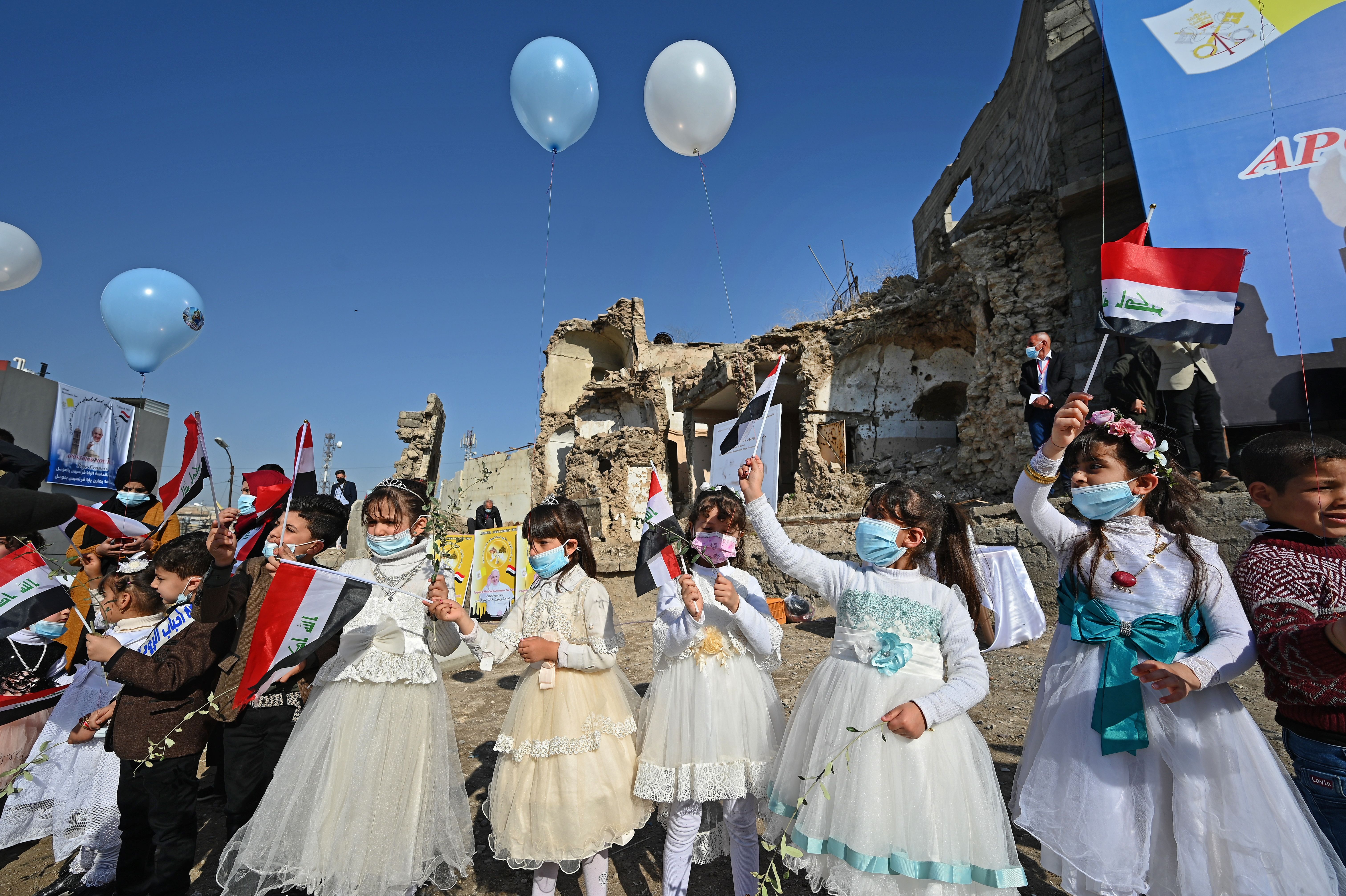 Iraqi children dressed in costumes wave national flags near the ruins of the Syriac Catholic Church of the Immaculate Conception, ahead of the Pope’s visit