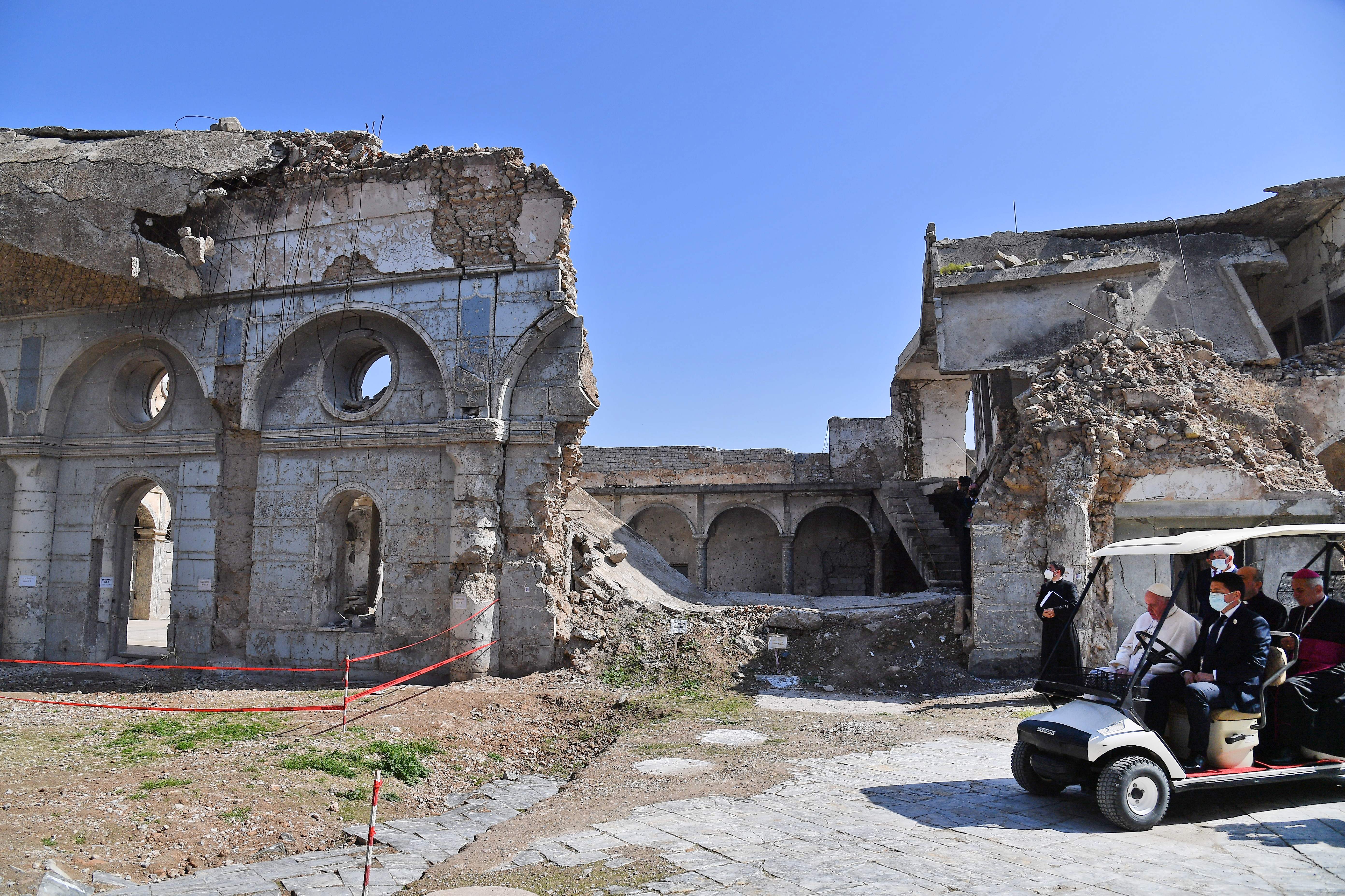 Pope Francis rides in a golf cart at the ruins of the Syriac Catholic Church of the Immaculate Conception