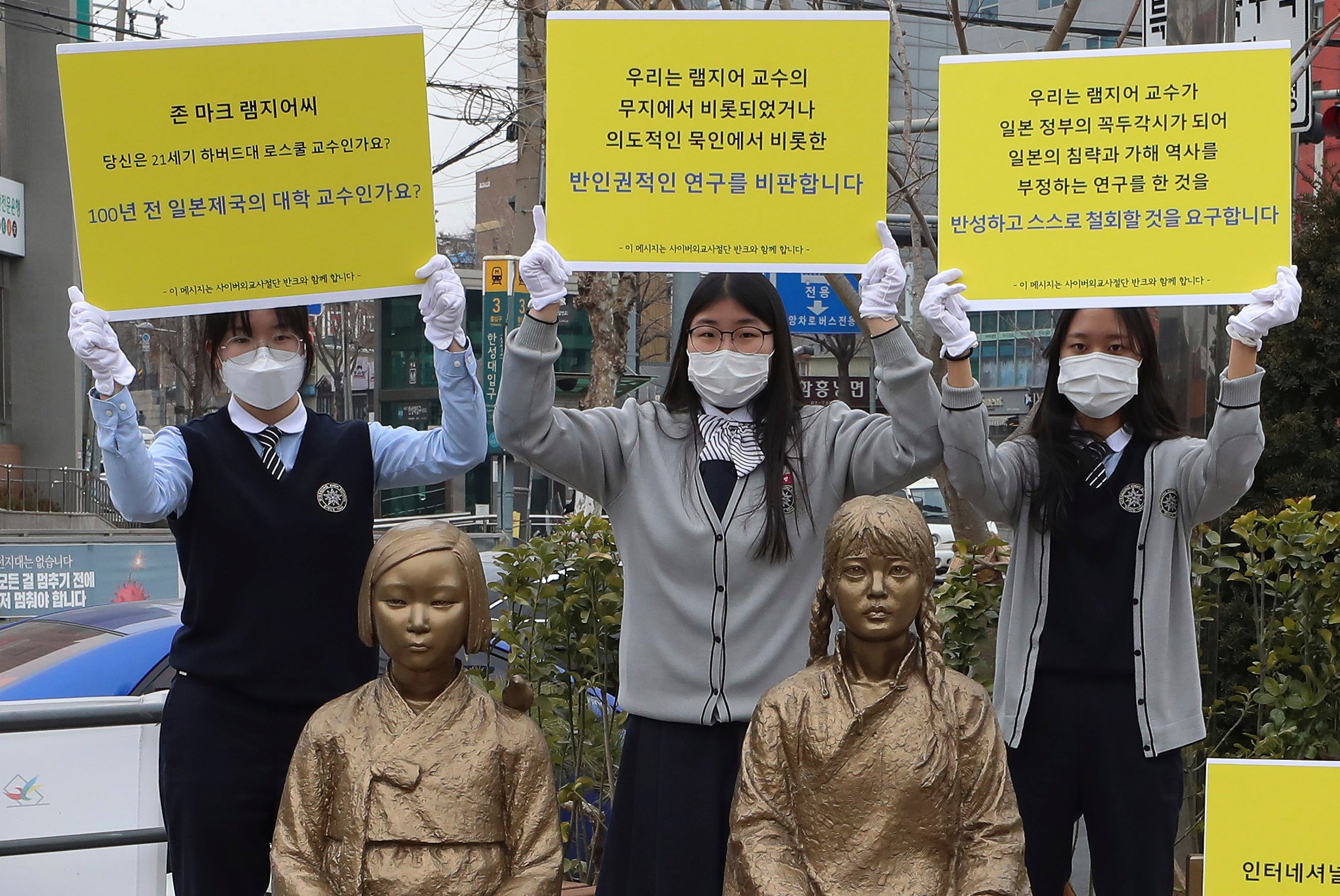 High school students hold up banners to protest a recent academic paper by Harvard University professor J Mark Ramseyer, behind statues symbolising wartime sex slaves in Seoul, South Korea